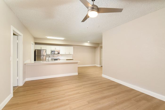 Modern open-floor apartment with sleek wooden flooring, minimalist kitchen featuring stainless steel appliances, and contemporary ceiling fan.