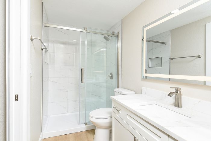 Elegant bathroom with a modern glass shower, sleek vanity, and bright LED mirror.