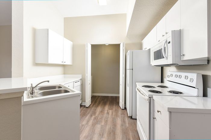 Sleek modern kitchen with pristine white cabinetry, stainless steel sink, and elegant wood flooring in a bright, inviting space.