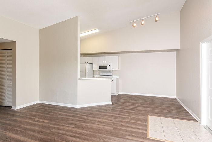 Bright, open-concept living space featuring stylish wood flooring and a modern kitchen with sleek white cabinetry and appliances.
