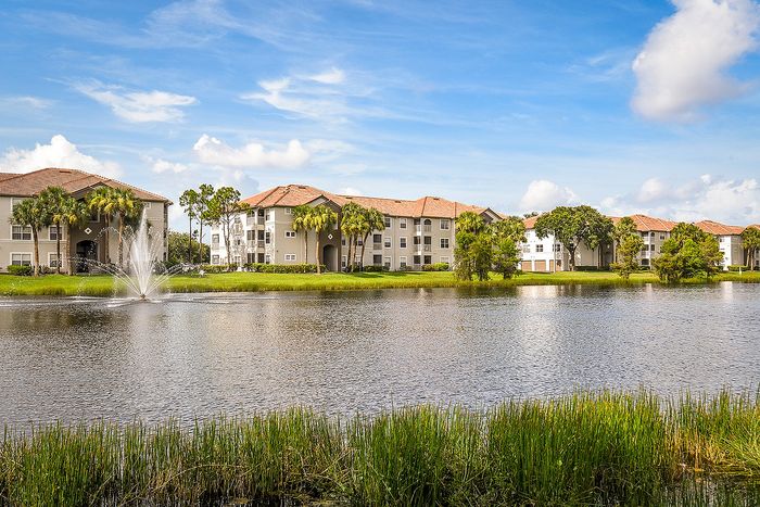 Charming lakeside apartments with elegant architecture, surrounded by lush greenery and a serene fountain view.