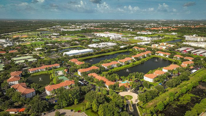Aerial view of a vibrant residential community with charming red-roofed buildings surrounded by lush greenery and serene lakes, perfect for modern living.