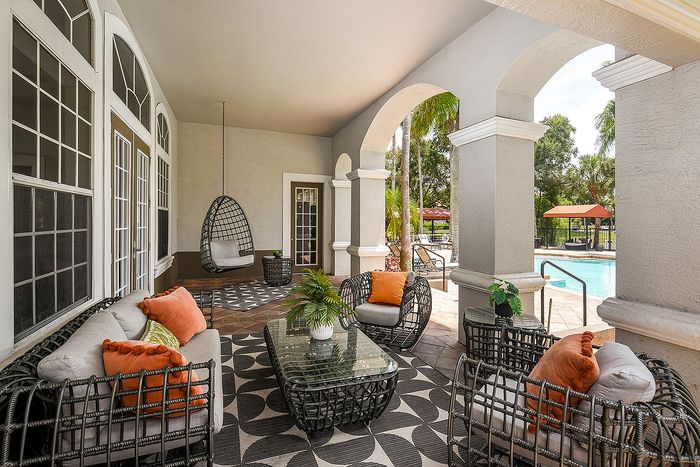 Inviting patio overlooking a sparkling pool, featuring chic wicker furniture and vibrant cushions, ideal for outdoor relaxation.