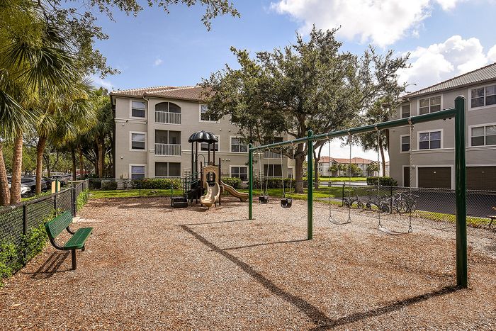 Inviting apartment playground with swings and slides, surrounded by lush greenery and modern buildings.