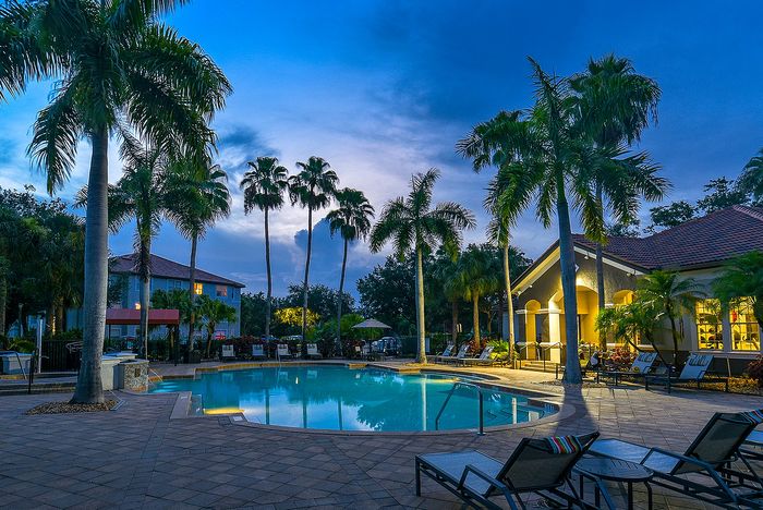 Charming apartment complex featuring a serene pool surrounded by lush palm trees and welcoming lounge chairs, perfect for relaxation and enjoying warm evenings.