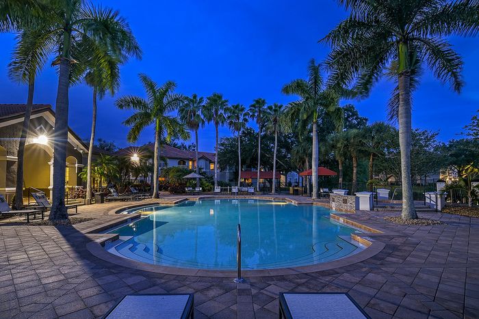 Luxurious resort-style pool area surrounded by tall palm trees and elegant seating, perfect for relaxation during twilight.