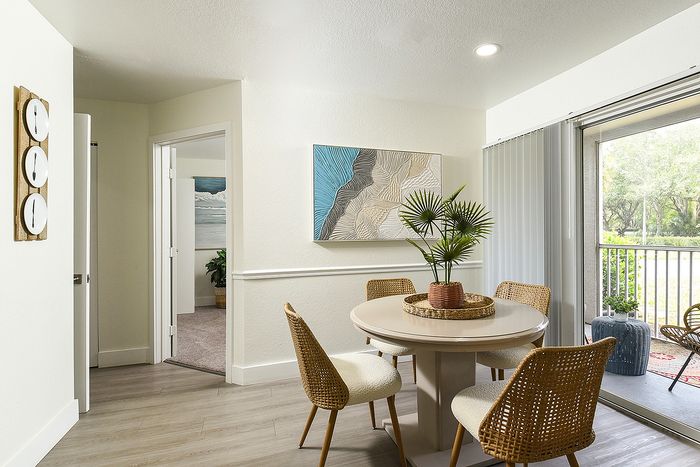 Bright dining area with chic wicker chairs and elegant decor, opening onto a scenic balcony view for a tranquil atmosphere.