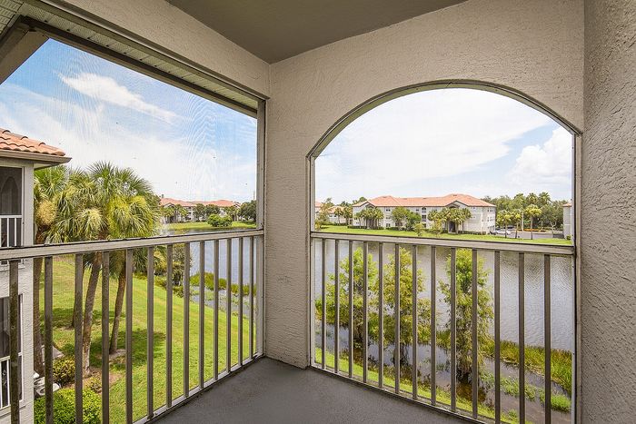 Charming balcony view overlooking a serene lake, with lush palm trees and elegant tiled rooftops in the background.