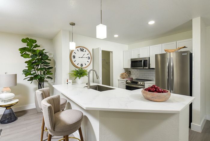 Modern kitchen with sleek countertops, elegant pendant lighting, and stainless steel appliances, enhanced by stylish decor and a vibrant indoor plant.