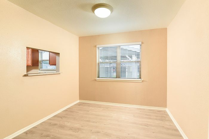 Bright and airy room with large window, sleek hardwood floors, and a charming pass-through to the kitchen.
