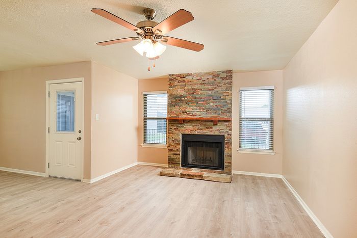 Inviting living room with modern ceiling fan, hardwood floors, and a charming stone fireplace.