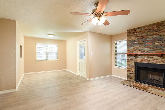 Inviting living room featuring elegant wood flooring, a charming stone fireplace, and natural light from large windows.