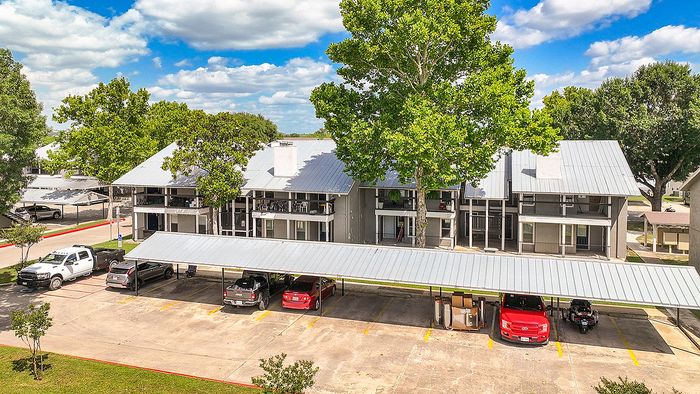 Inviting apartment complex featuring modern design, surrounded by lush green trees, with convenient covered parking under a clear blue sky.