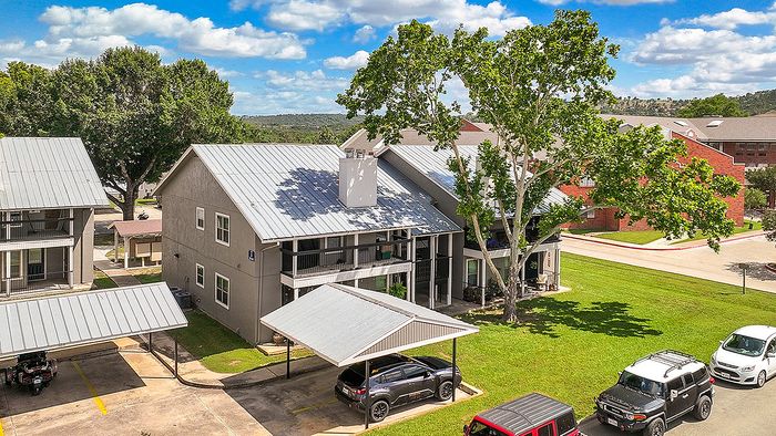 Charming apartment complex with modern gray exteriors, lush trees, and convenient covered parking. Scenic views and open, green spaces make this a desirable living environment.