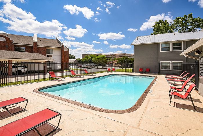 Inviting apartment community pool with bright red lounge chairs under a clear blue sky, perfect for relaxation and leisure.