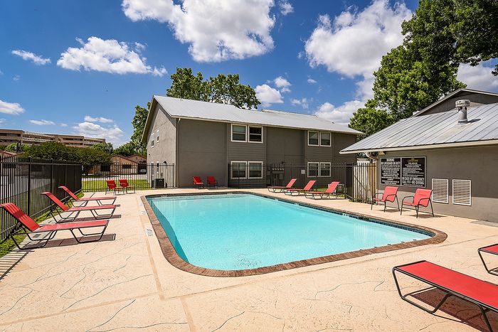 Inviting outdoor pool with red lounge chairs, sunny skies, and lush greenery, perfect for relaxation.
