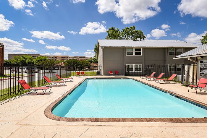Inviting outdoor pool area with vibrant red lounge chairs and spacious surroundings, perfect for relaxation and enjoyment under a clear blue sky.