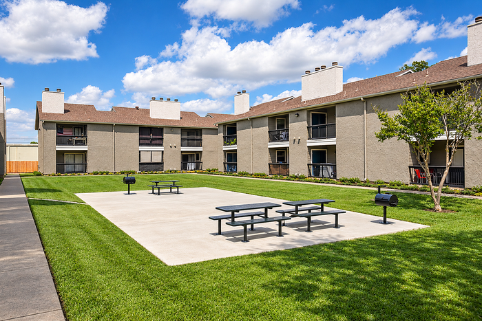 Charming apartment complex with spacious grassy courtyard, picnic tables, and barbecue grills under a clear blue sky.