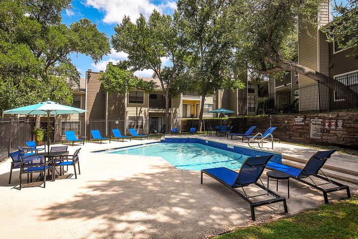 Inviting outdoor pool area with blue lounge chairs, shaded tables, and lush greenery for a relaxing retreat.