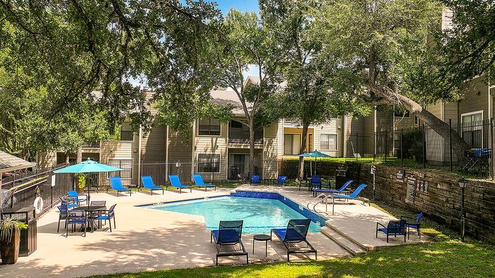 Charming apartment complex with lush greenery and a refreshing outdoor pool area featuring stylish lounge chairs and umbrellas.