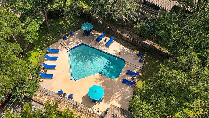Inviting community swimming pool surrounded by lush greenery, featuring multiple blue loungers and a shaded seating area.