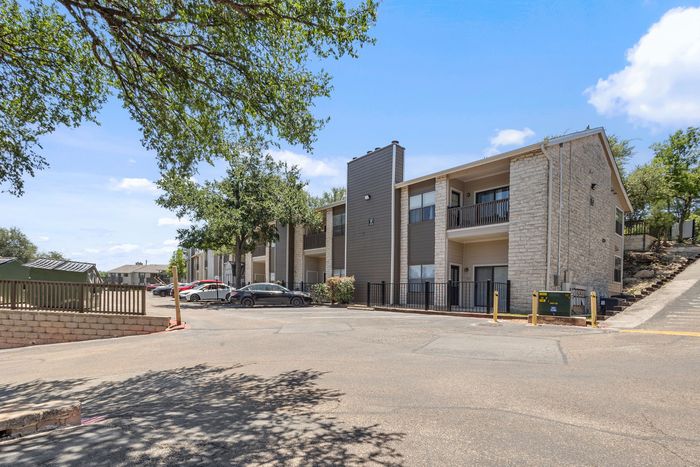 Charming apartment complex with modern exterior, ample parking, and lush greenery under a clear blue sky.