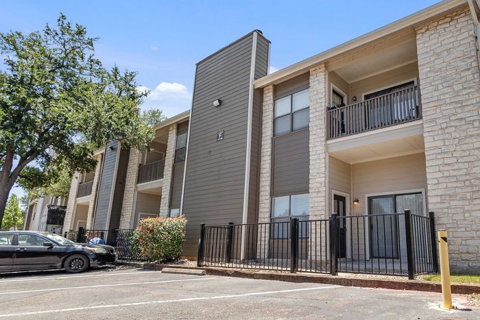 Inviting apartment complex with stone accents and spacious balconies, nestled among lush greenery for serene living.