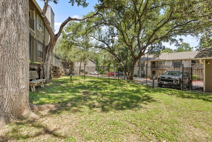 Charming outdoor space with lush green lawn, mature trees, and inviting seating area in a peaceful apartment complex setting.