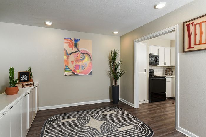 Charming apartment entryway with vibrant artwork, stylish rug, and view into a modern kitchen.