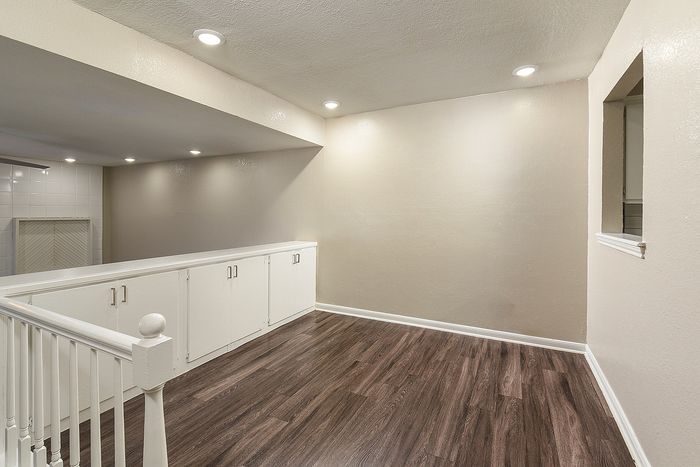 Bright and modern empty room with elegant wood flooring, recessed lighting, and a built-in cabinet, offering a sleek and versatile living space.