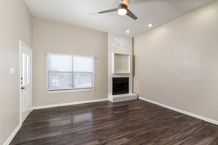 Bright and modern living room with sleek laminate flooring, a stylish ceiling fan, and an elegant white tiled fireplace.