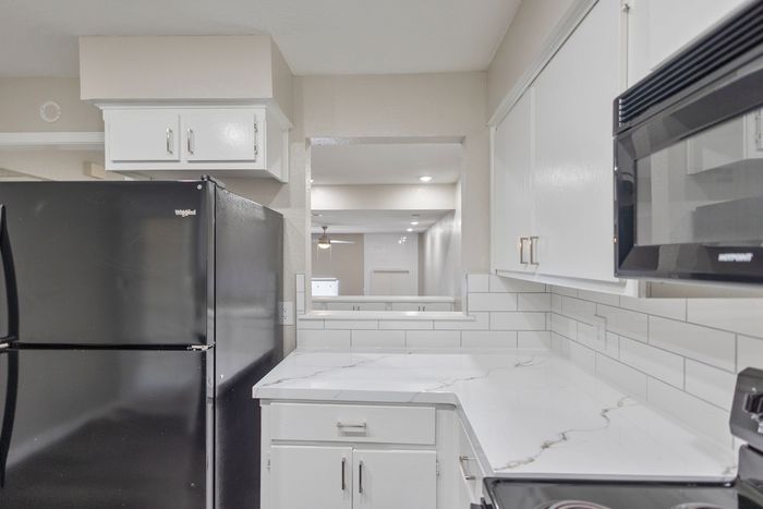 Modern kitchen with sleek black appliances, white cabinetry, and marble-patterned countertops.