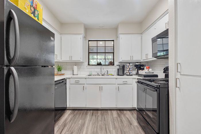 Modern kitchen featuring sleek black appliances, elegant white cabinetry, and stylish wood flooring, perfect for culinary adventures.