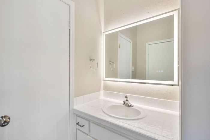 Modern bathroom with sleek mirror lighting and a pristine white countertop featuring a stylish sink design.