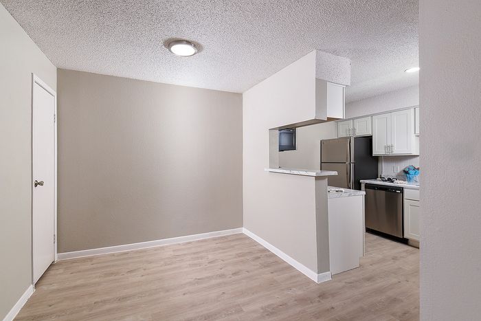 Chic apartment interior featuring a cozy corner with sleek laminate flooring and a modern kitchen view through a convenient serving hatch.