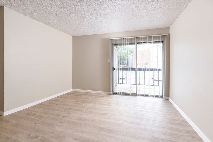 Bright and airy living room with stylish wood flooring and large sliding glass doors leading to a balcony, offering abundant natural light.