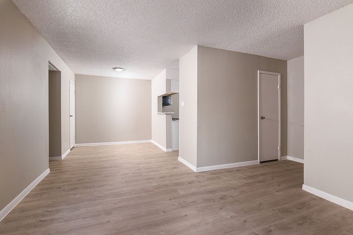 Modern apartment interior with sleek wood flooring, neutral walls, and open layout featuring a compact kitchen area.