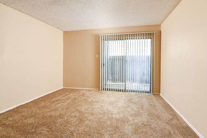 Bright and spacious room with plush carpet and large sliding glass door, perfect for natural light.