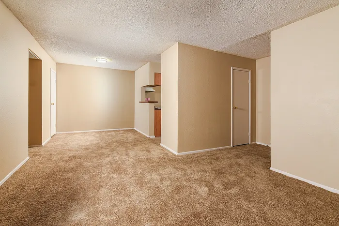 Spacious empty room with warm beige walls, plush carpeting, and a cozy nook perfect for a small dining area or home office.