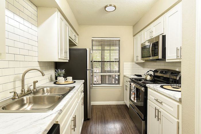 Contemporary kitchen with sleek white cabinetry, stainless steel appliances, and elegant wood flooring, infused with natural light.