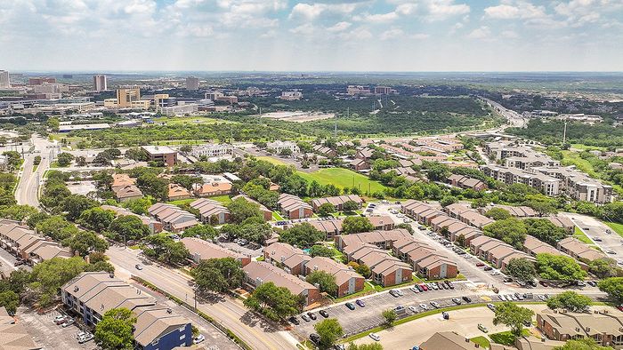 Aerial view of a vibrant residential community surrounded by lush greenery and expansive cityscape, showcasing modern living in a serene environment.