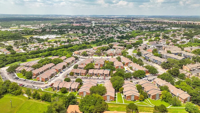 Expansive aerial view of a beautifully planned apartment community surrounded by lush greenery and picturesque hills, ideal for a tranquil lifestyle.