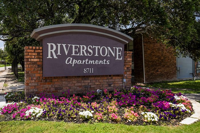 Charming entrance to Riverstone Apartments featuring lush landscaping and vibrant flowers, offering a warm and inviting welcome.
