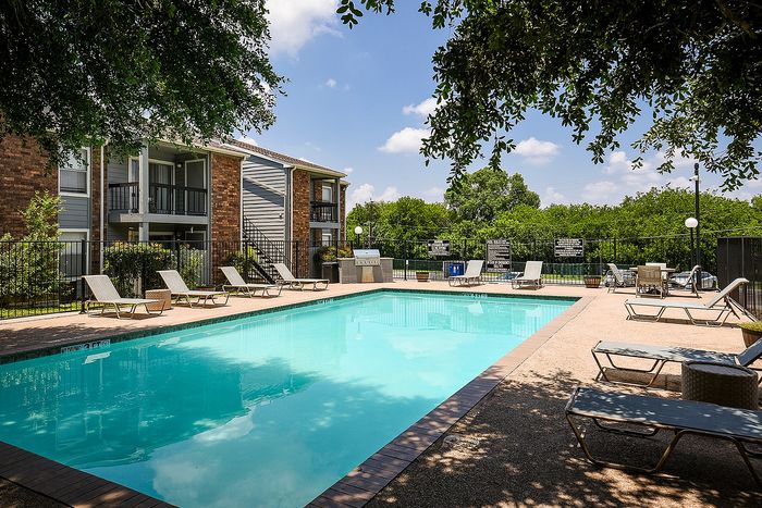 Inviting outdoor pool area with sun loungers and lush greenery, perfect for relaxation in a tranquil apartment community.