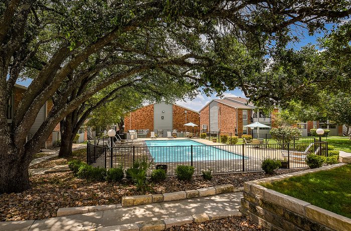 Charming apartment complex featuring a sunlit swimming pool surrounded by lush greenery and cozy lounge areas.