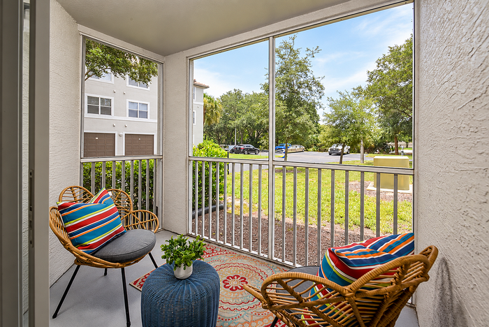 Charming screened-in patio featuring cozy seating, vibrant cushions, and a view of lush greenery in a serene apartment complex.