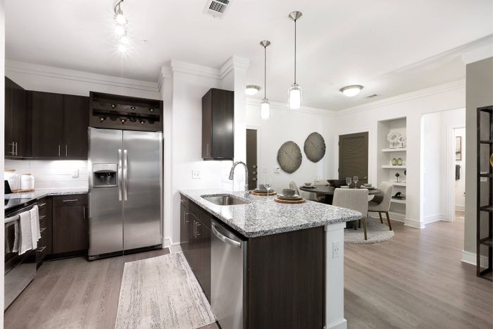 Open-concept kitchen with granite countertops, stainless steel appliances, and view of dining area at The Adley Craig Ranch apartments for rent