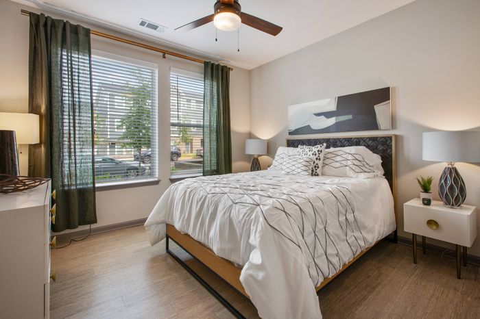 Furnished bedroom with ceiling fan and windows for natural light at Solis City Park apartments for rent