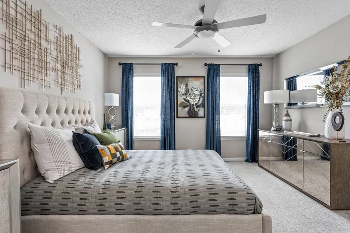 Spacious bedroom with plush carpeting, tall windows, and ceiling fan