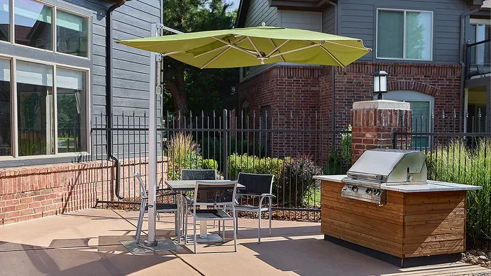 Charming outdoor patio featuring a modern grill, dining set, and green parasol, perfect for entertaining.
